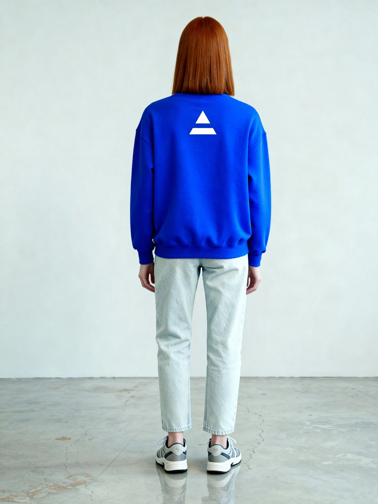 Back view of female model wearing the royal blue sweatshirt with the minimalist white triad logo printed at the upper back.